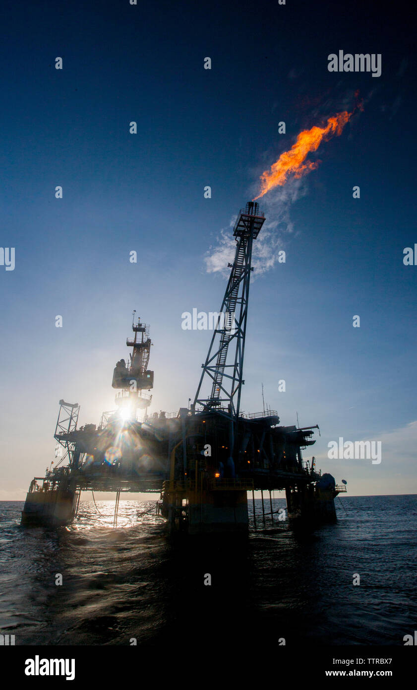 Oil rig in sea emitting fire on sunny day Stock Photo