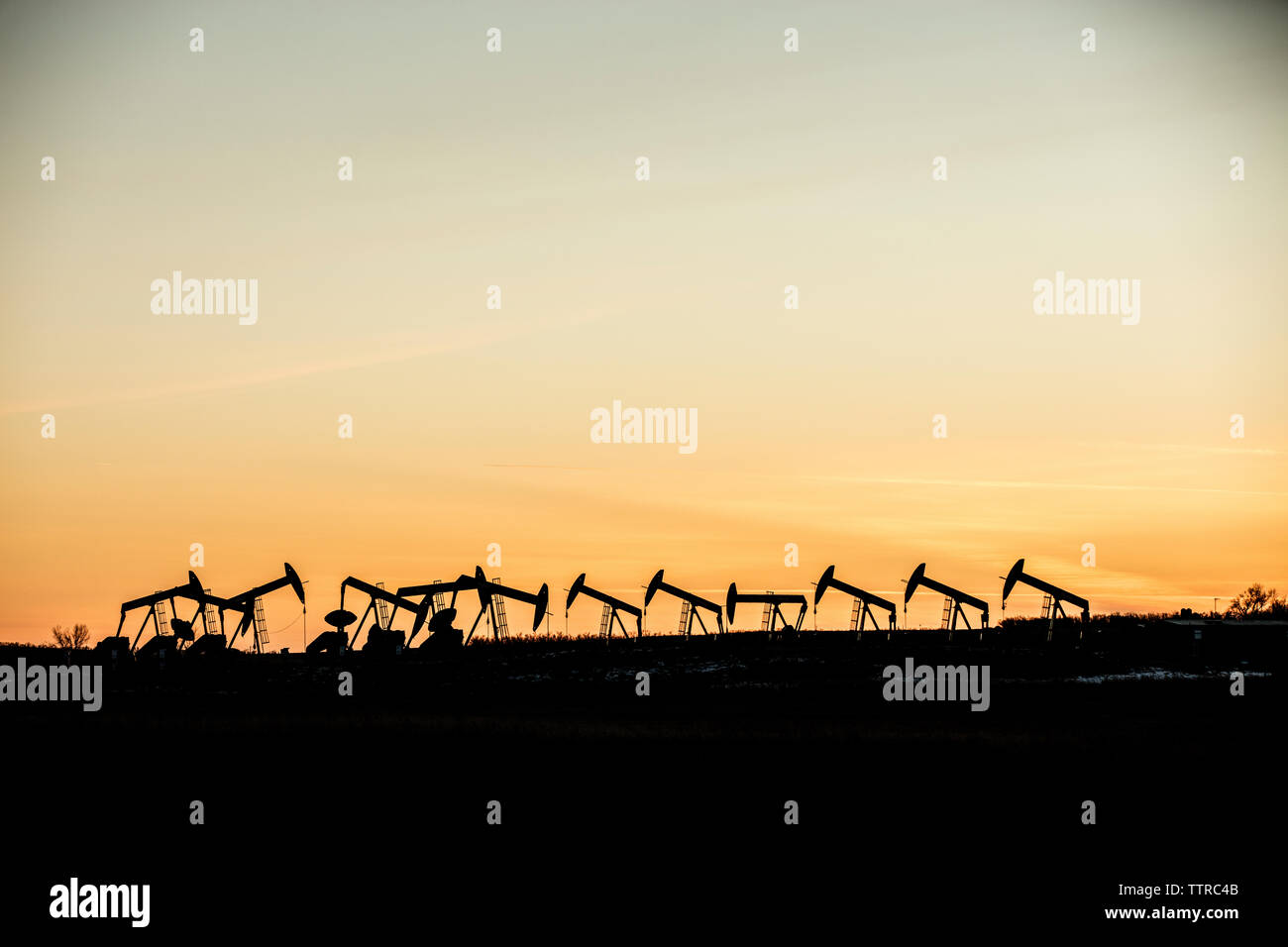 Mid distance view of silhouette pumpjacks at oil industry against sky during sunset Stock Photo
