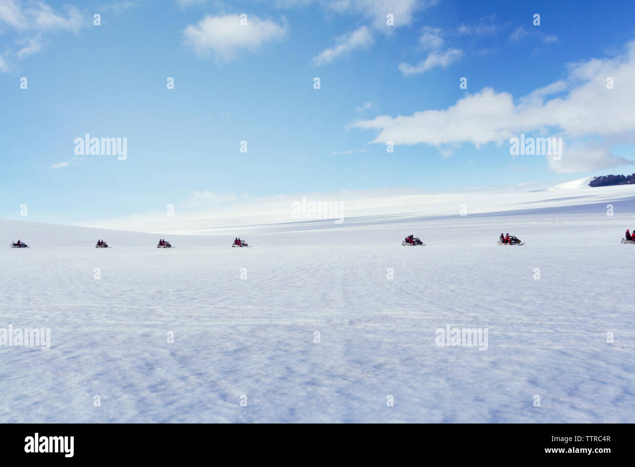 Mid distance of people riding snowmobiles on landscape against blue sky Stock Photo