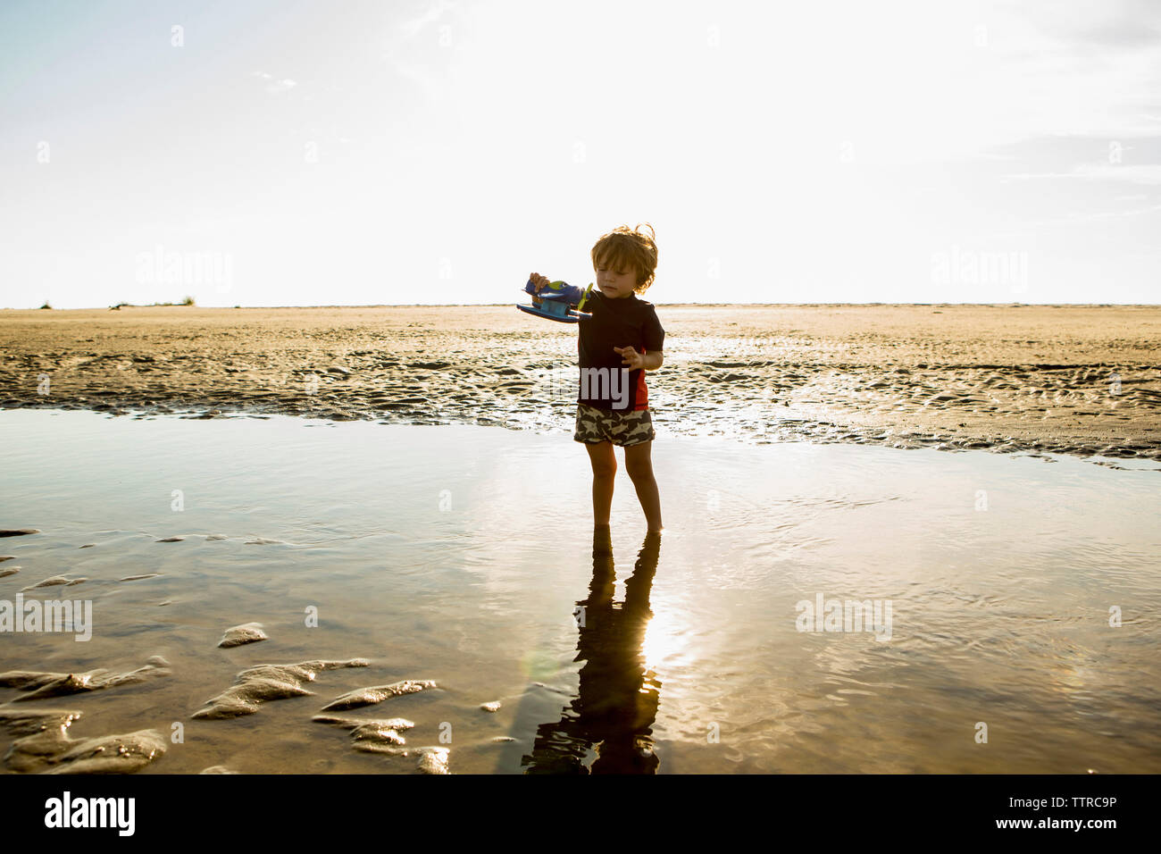 Boy playing with toy while standing in water at beach Stock Photo