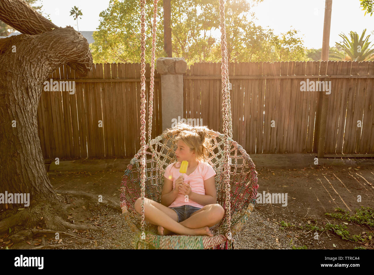 Girl looking away while holding popsicle on swing Stock Photo