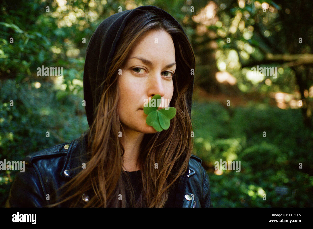 Portrait of woman with clover leaves in mouth in forest Stock Photo