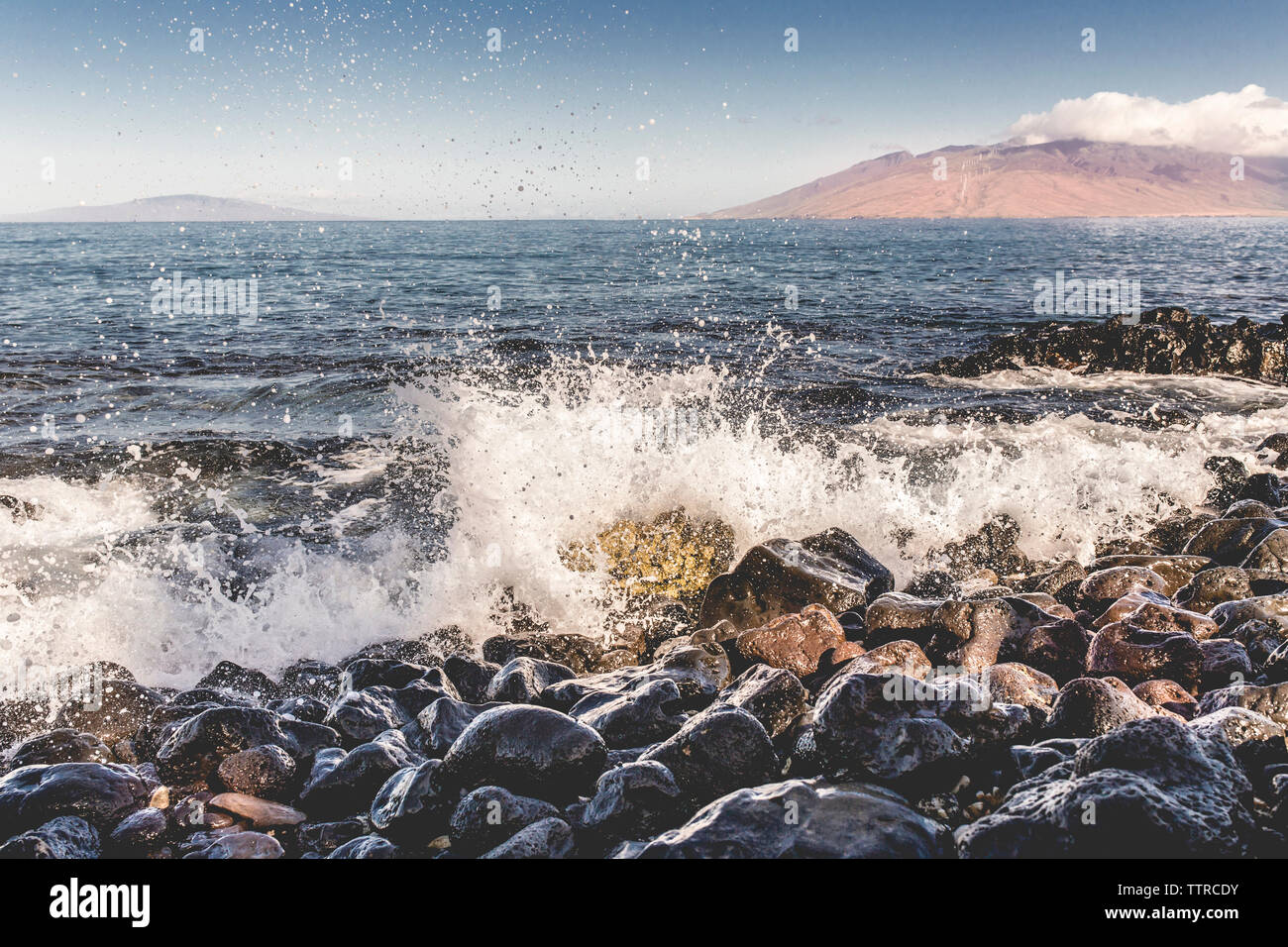 Waves splashing on rocks at shore against sky Stock Photo