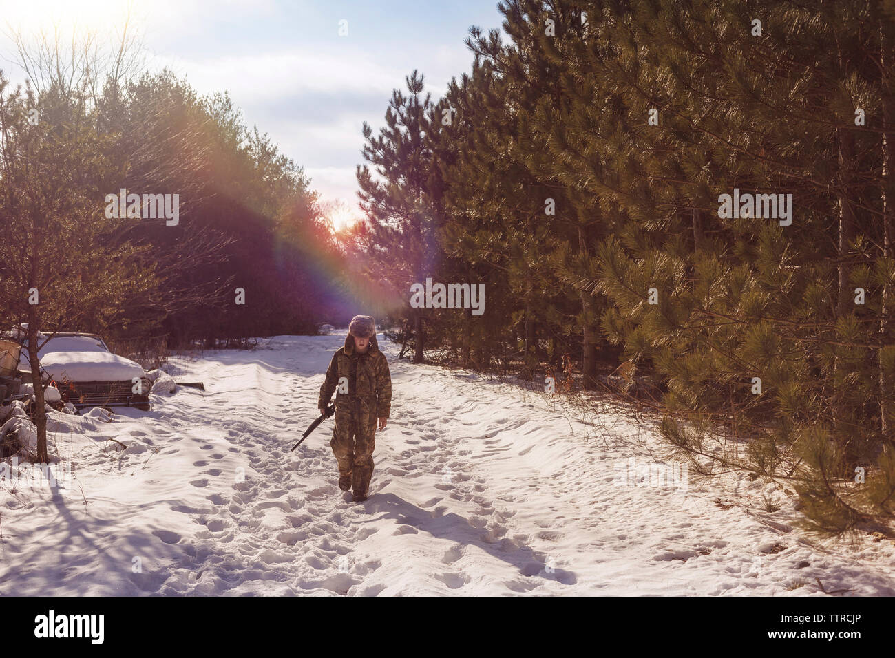 Full length of boy holding gun walking on snow covered field amidst trees Stock Photo