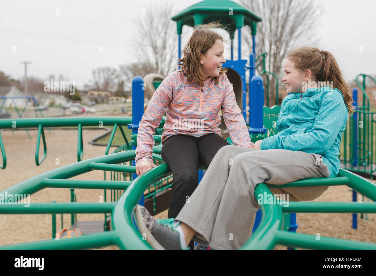 Friends talking while sitting on jungle gym at playground Stock Photo
