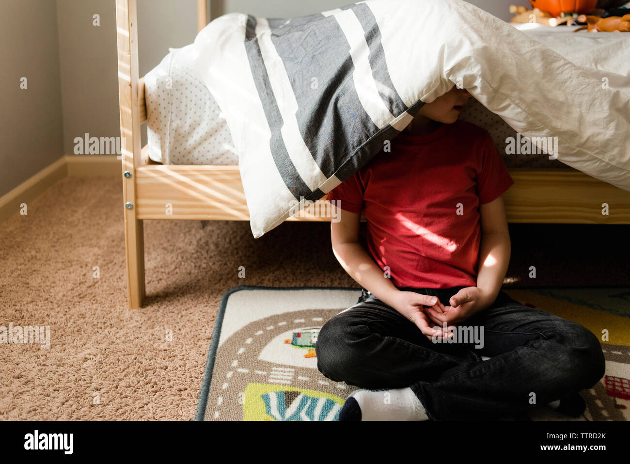 Boy sitting against bunkbed with blanket on head Stock Photo