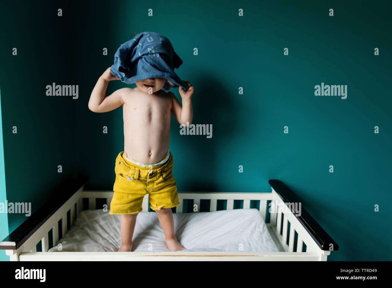 Boy removing shirt while standing in bunkbed against wall Stock Photo