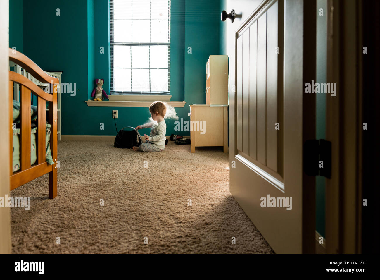 Boy playing with steam machine while sitting on rug at home seen through doorway Stock Photo