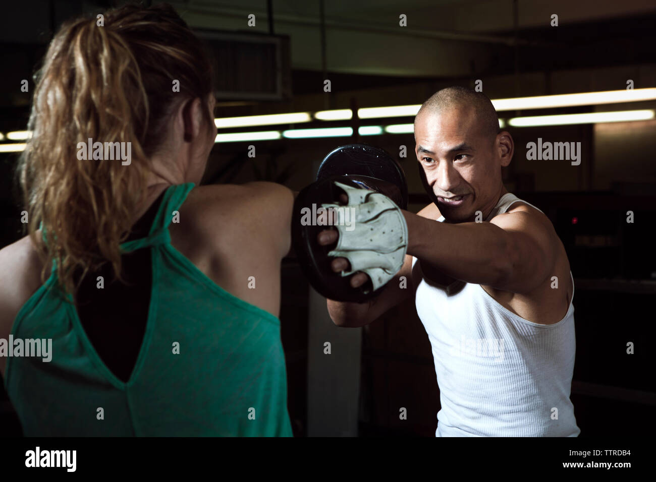 Smiling trainer assisting female boxer in boxing ring at gym Stock Photo