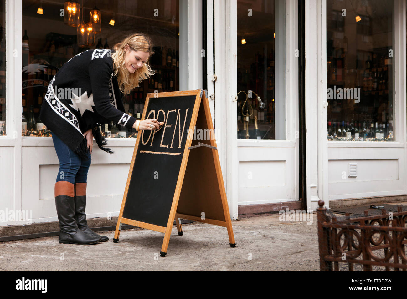 female small business owner making open sign outside wine shop Stock Photo