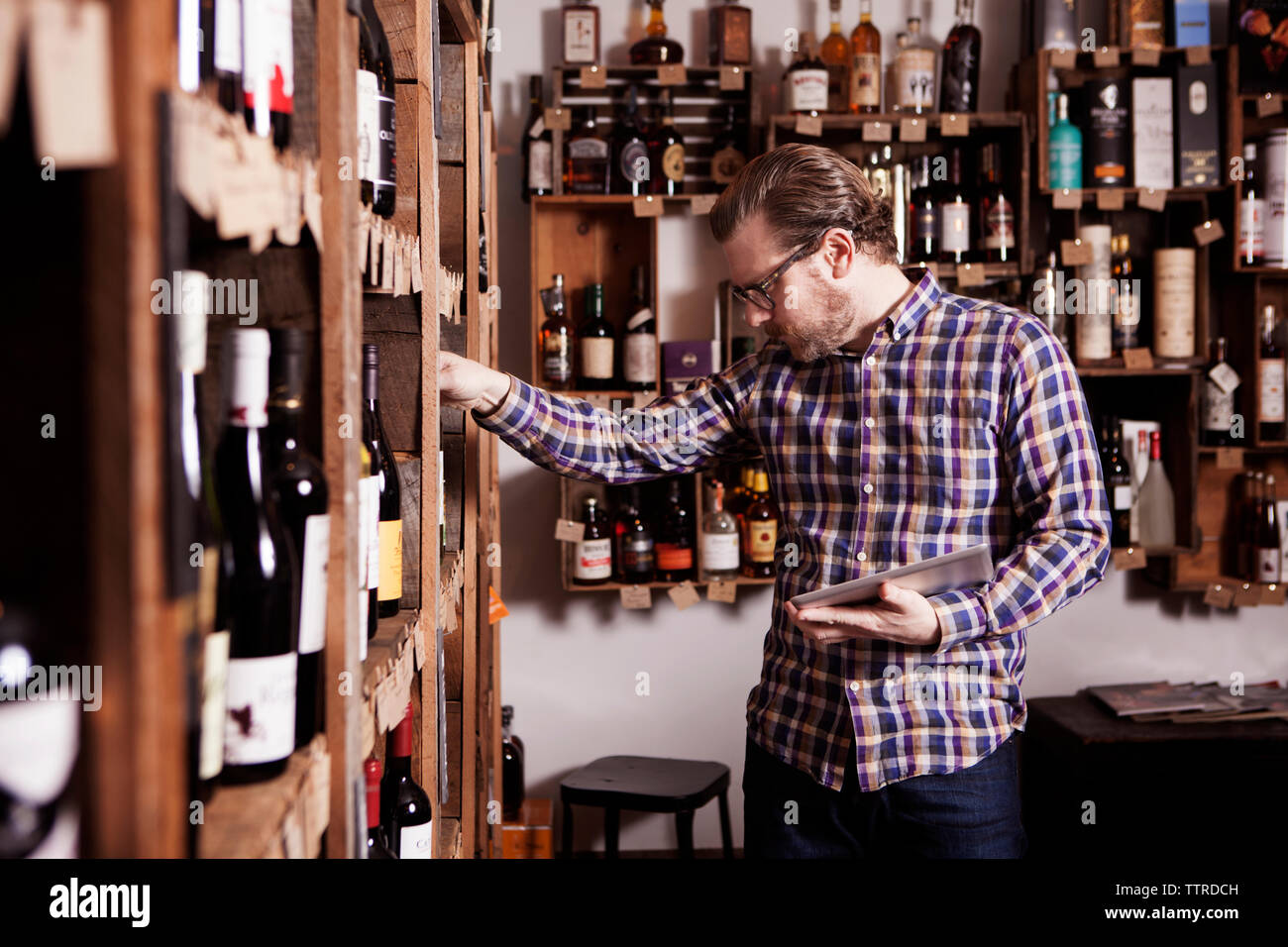 Male small business owner examining wine bottle while holding tablet computer in shop Stock Photo