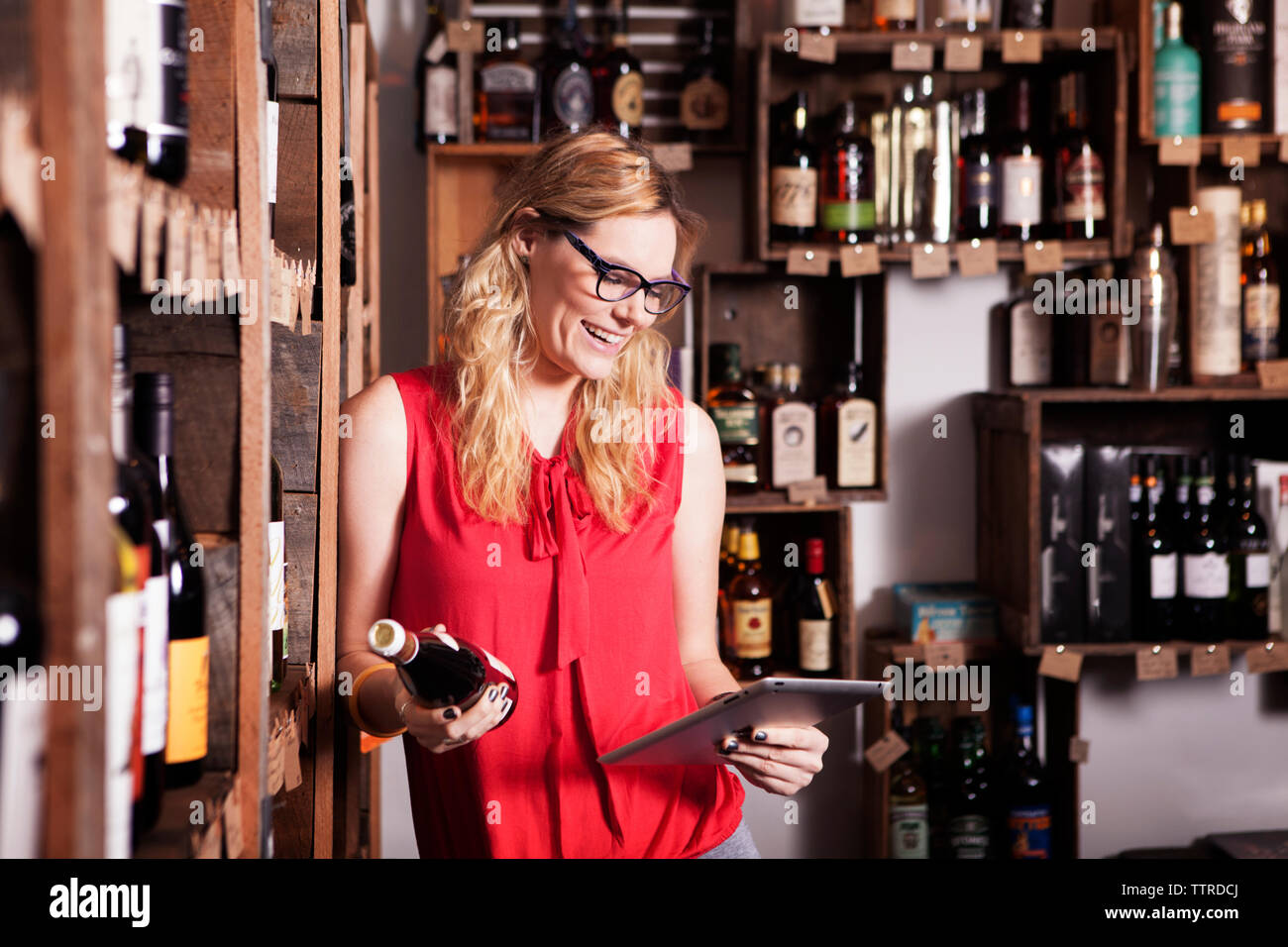 Happy female entrepreneur using tablet computer while holding wine bottle in shop Stock Photo