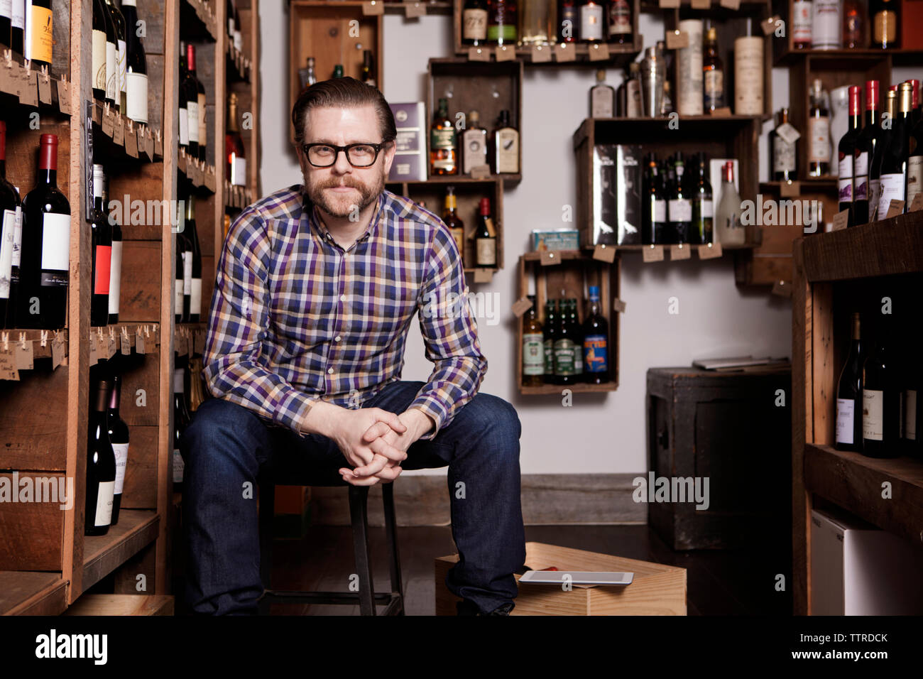 Portrait of confident male owner sitting with hands clasped in wine shop Stock Photo