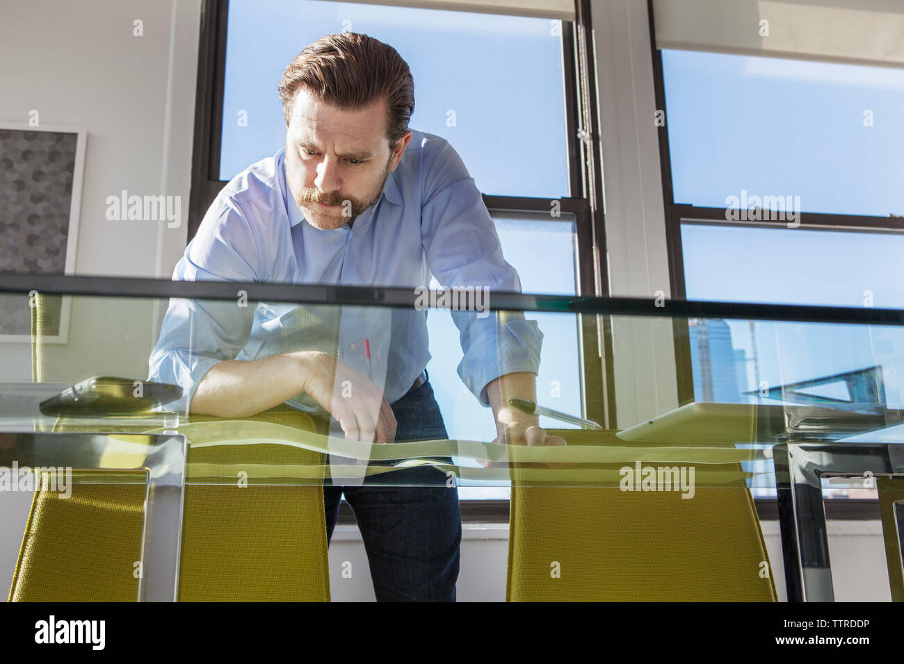Low angle view of businessman analyzing photographs at glass conference table in creative office Stock Photo