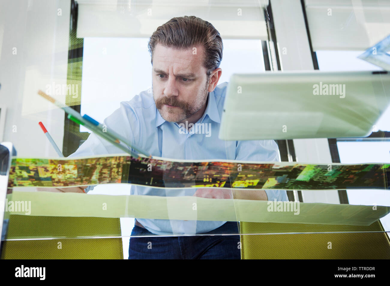 Low angle view of creative businessman analyzing photographs at glass conference table Stock Photo