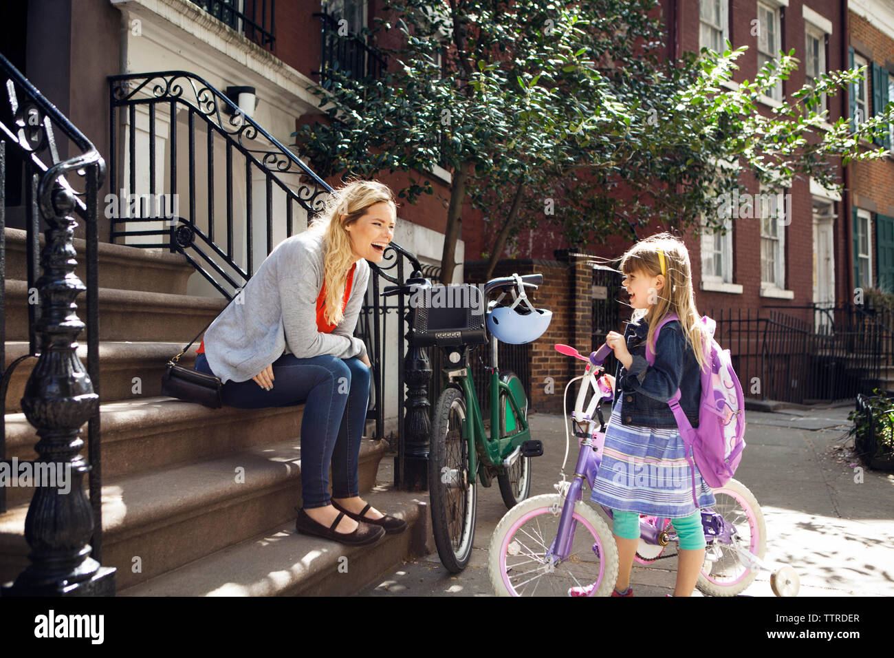 Cheerful mother and daughter with bicycles talking on steps Stock Photo