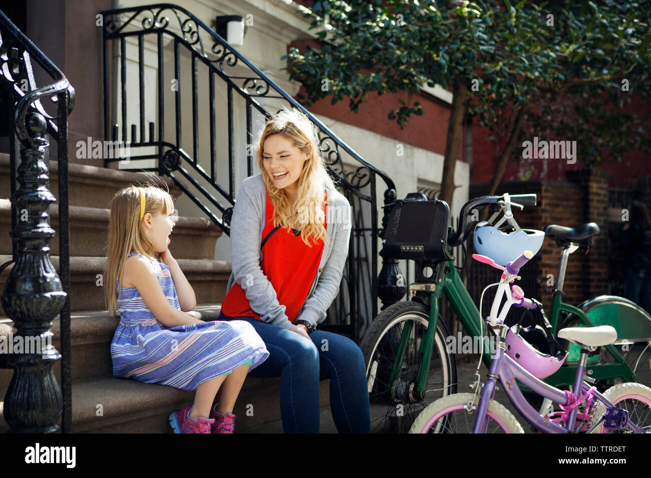 Happy mother and daughter talking on steps with bicycles parked in foreground Stock Photo