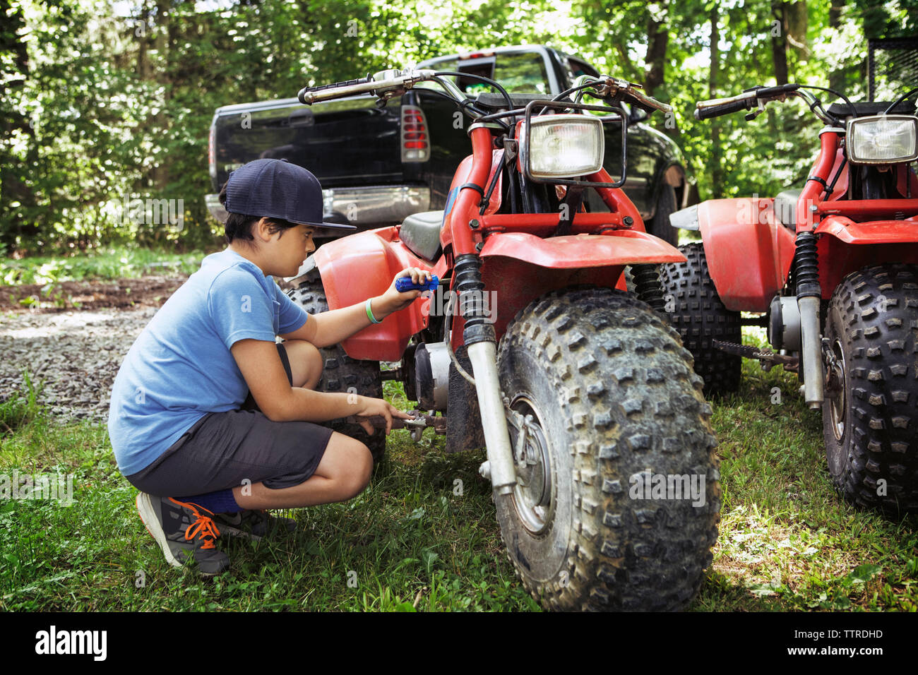 Boy repairing ATV on grass field Stock Photo