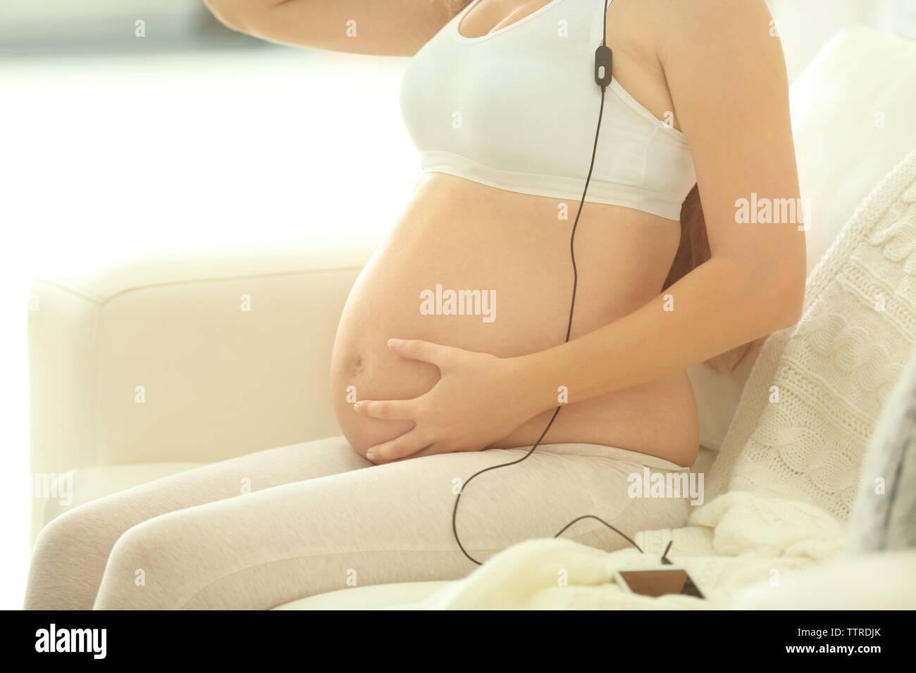 Young pregnant woman listening to music on the sofa Stock Photo - Alamy