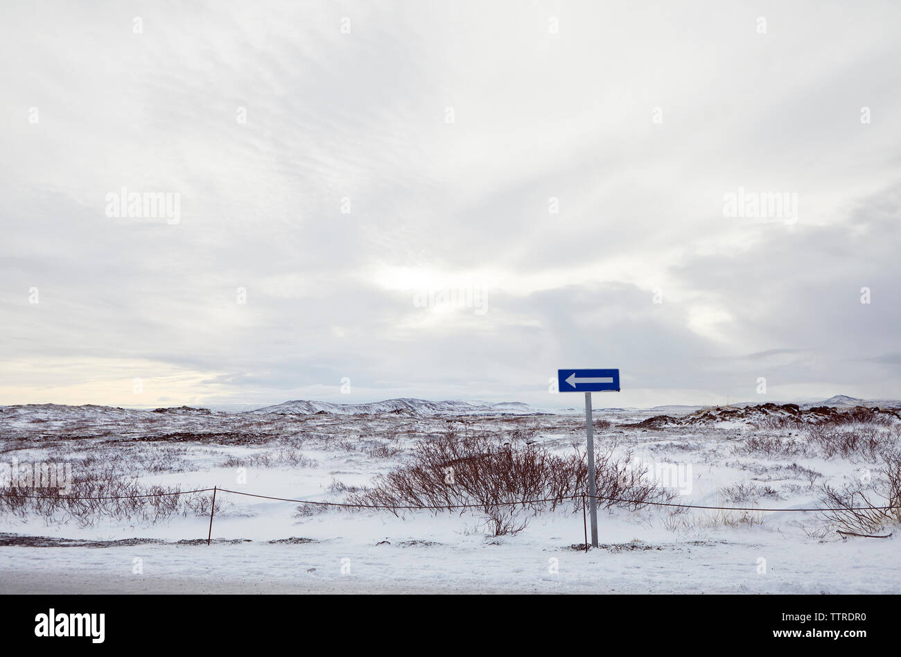Arrow symbol on snow covered landscape against cloudy sky Stock Photo