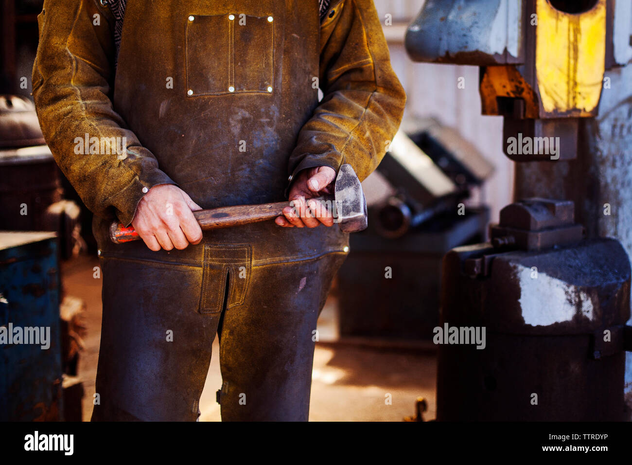 Midsection of craftsperson holding hammer at metal industry Stock Photo