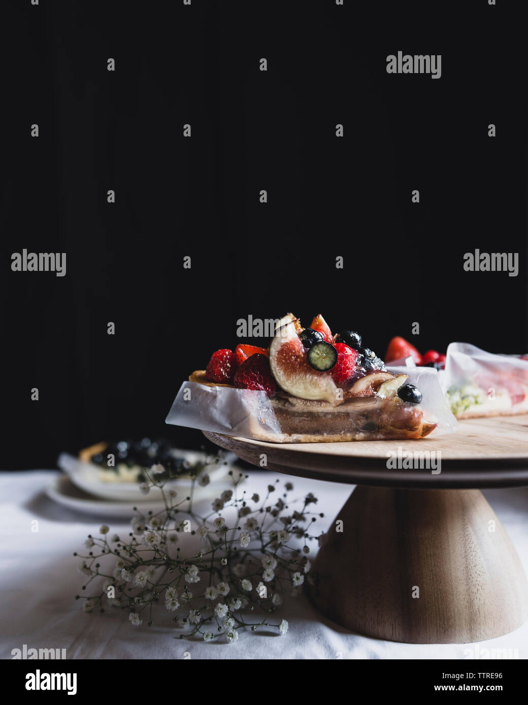 Tart on cakestand on table against black wall Stock Photo