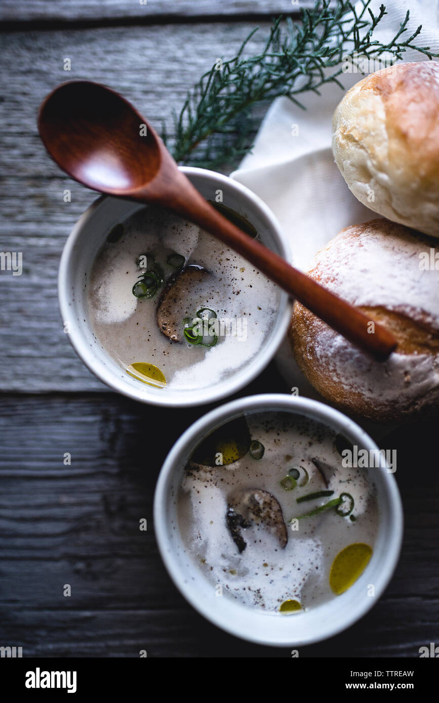 Overhead shot of mushroom soup with spoon and buns on wooden table Stock Photo