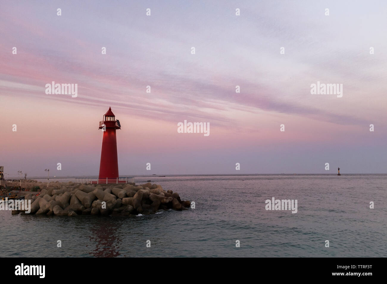 Red lighthouse on pier by sea against sky during dusk Stock Photo