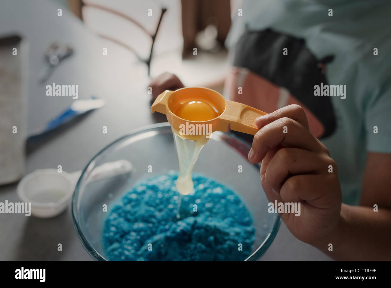 Cropped hand of boy filtering egg white in bowl while preparing food Stock Photo