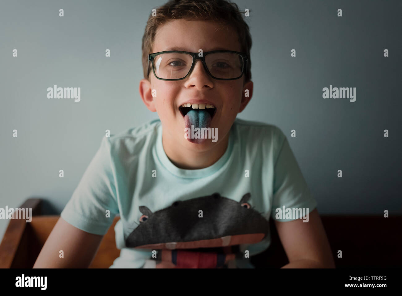 Portrait of playful boy sticking out tongue against wall at home Stock Photo