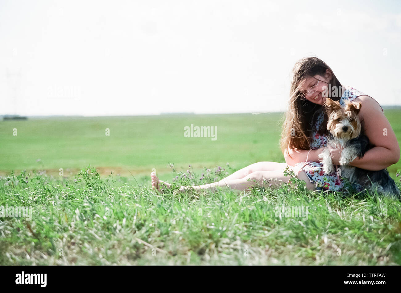 Full length of overweight teenage girl playing with Yorkshire Terrier on grassy field against clear sky during sunny day Stock Photo