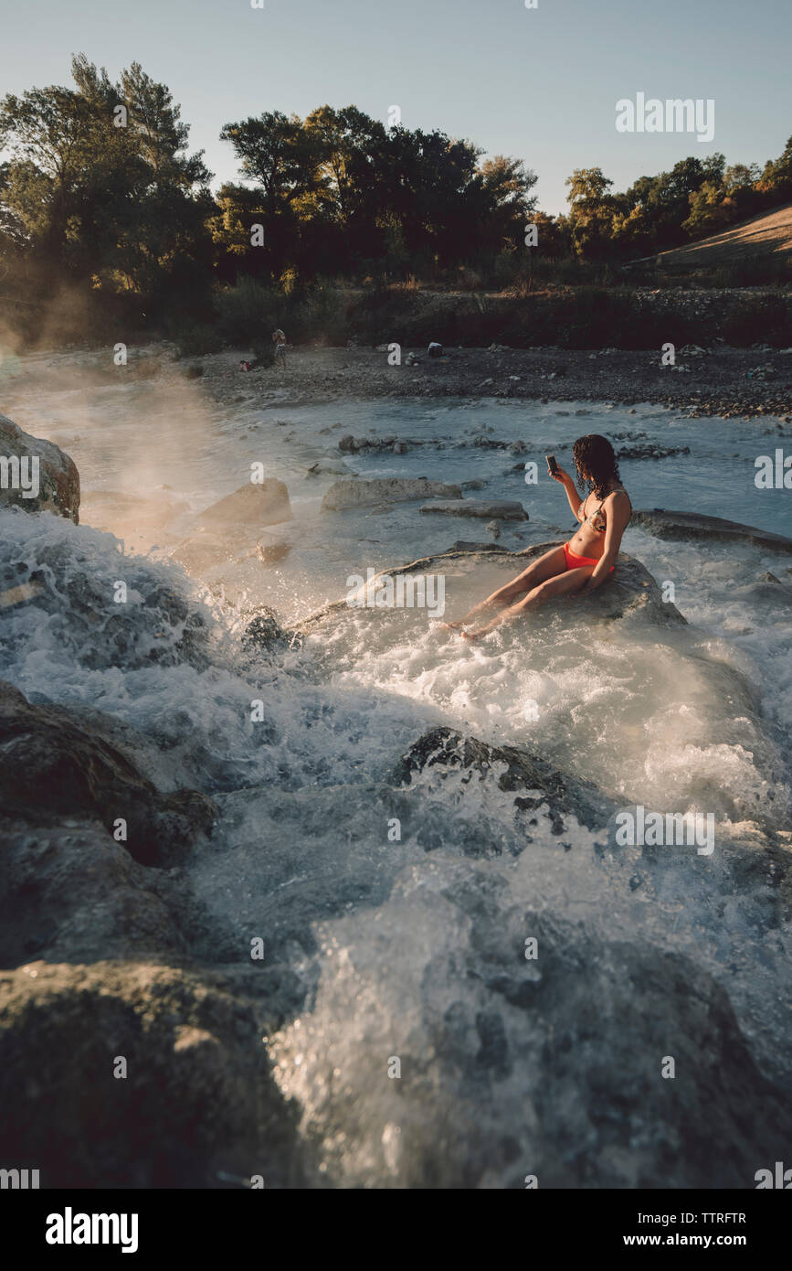 High angle view of woman sitting on rocks while enjoying in steam emitting thermal pool Stock Photo