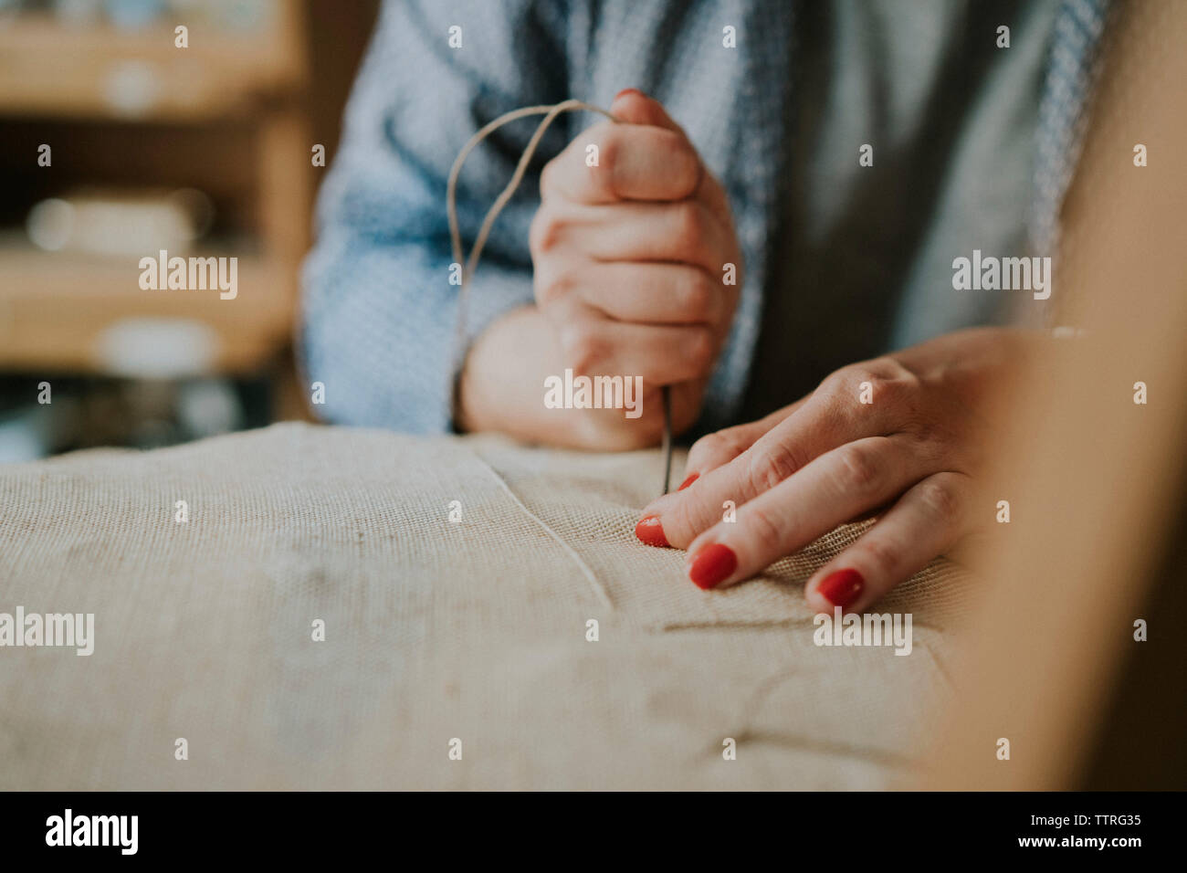 Midsection of female upholsterer stitching fabric on chair in workshop Stock Photo