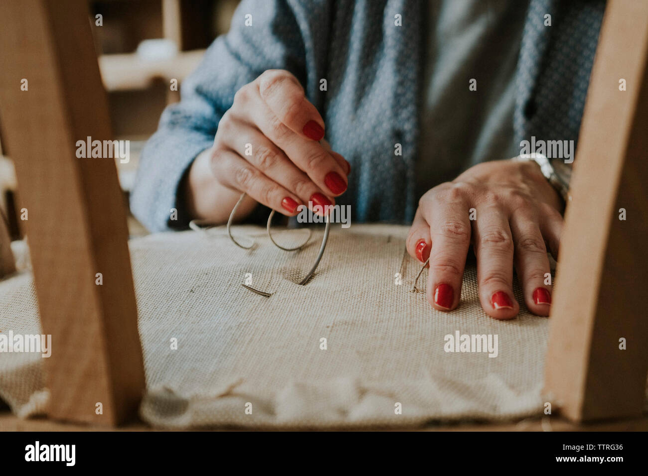 Midsection of upholsterer stitching fabric on chair in workshop Stock Photo