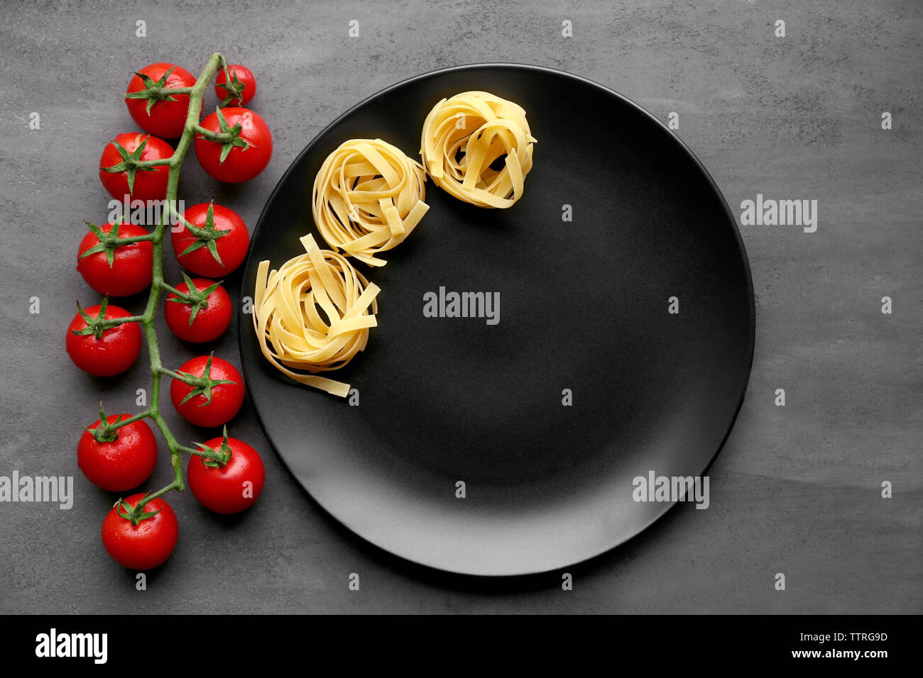 Cherry tomatoes and pasta with black plate on table Stock Photo