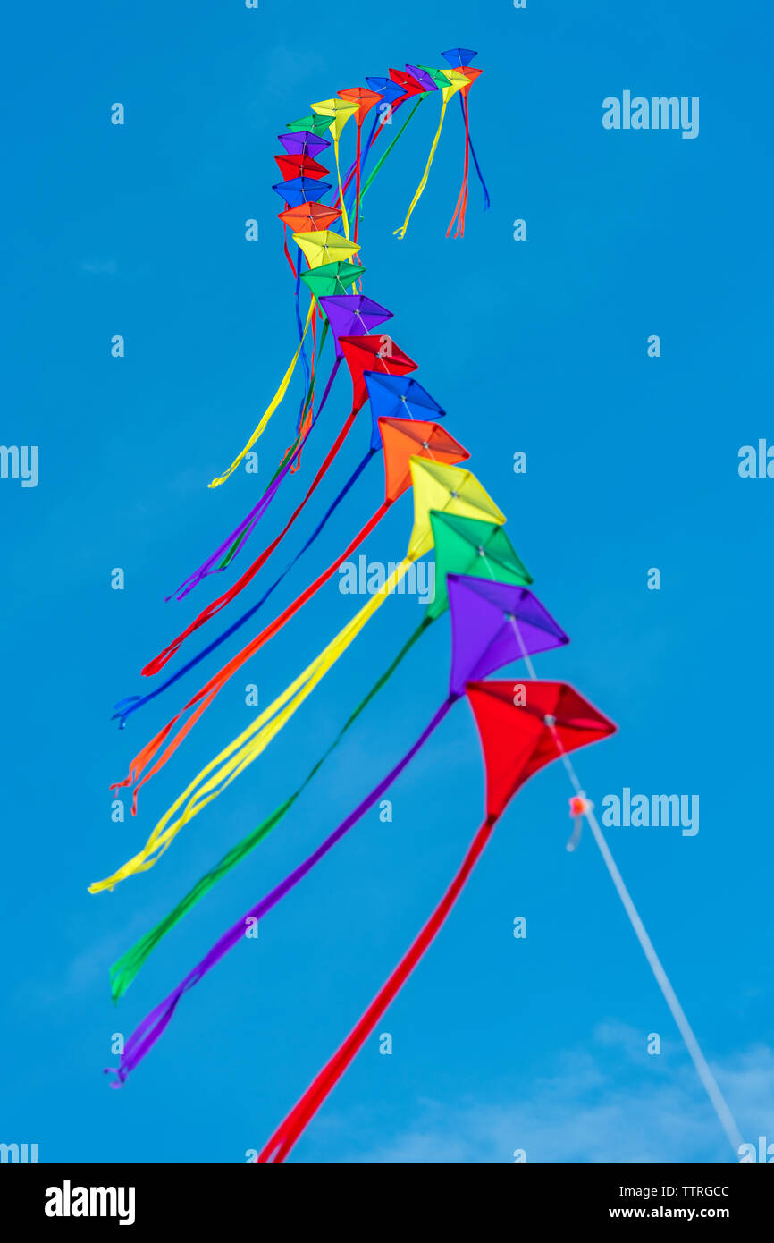 A row of colourful kites on a single line against a clear blue sky. Stock Photo