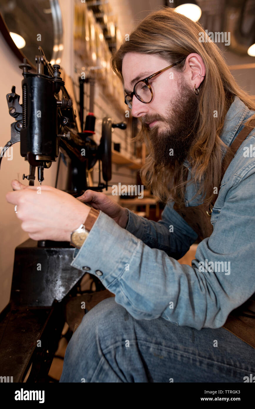 Serious shoemaker stitching leather at workshop Stock Photo