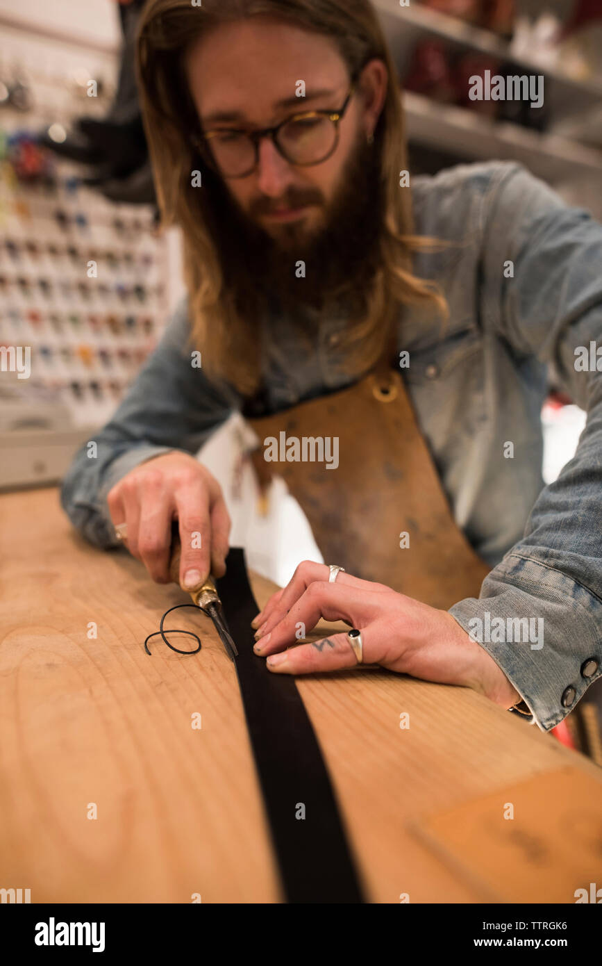 Shoemaker cutting leather on workbench at workshop Stock Photo