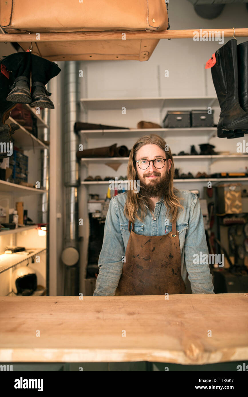Portrait of smiling shoemaker standing at workbench in workshop Stock Photo