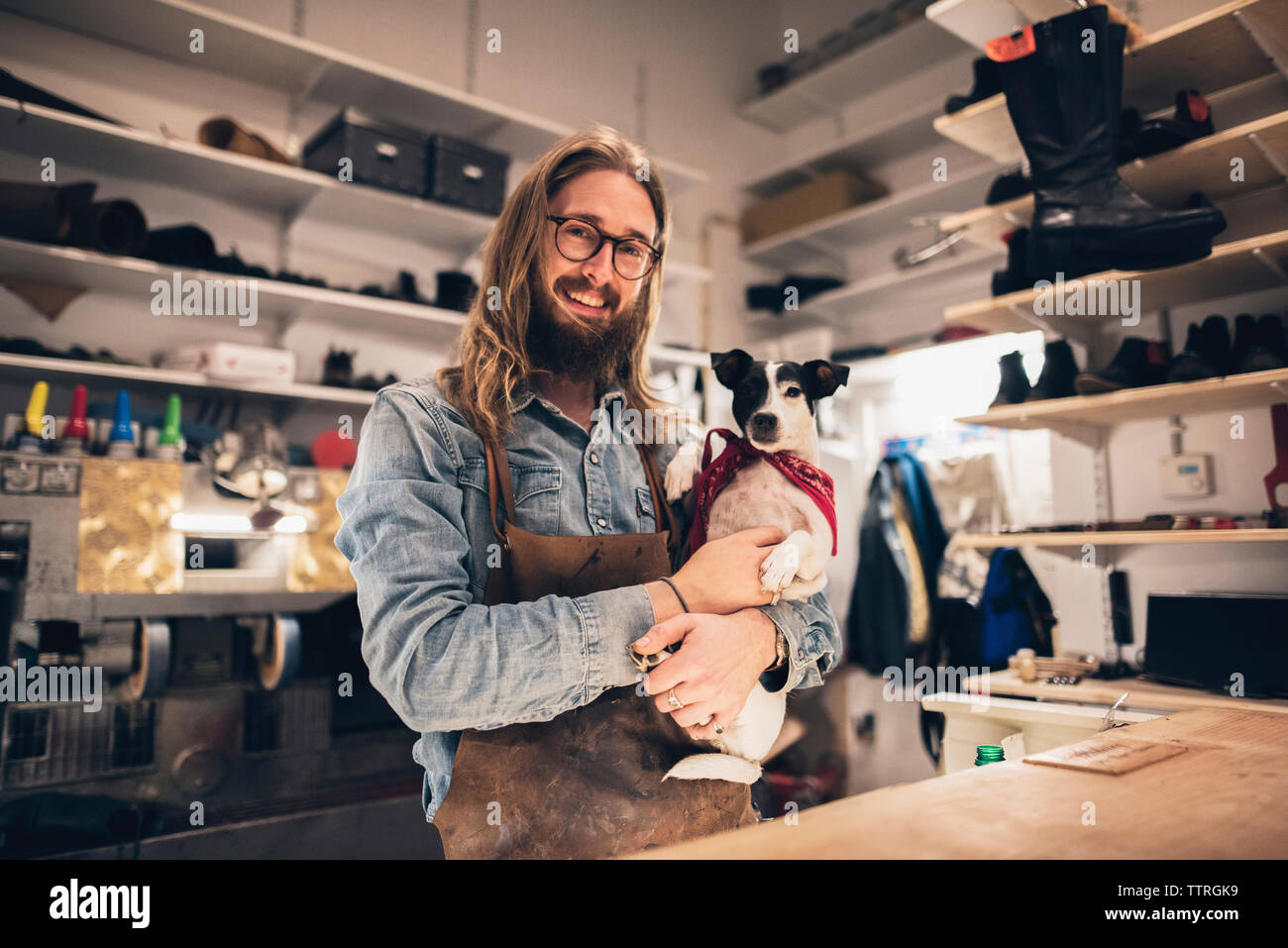 Portrait of smiling shoemaker carrying dog at workshop Stock Photo