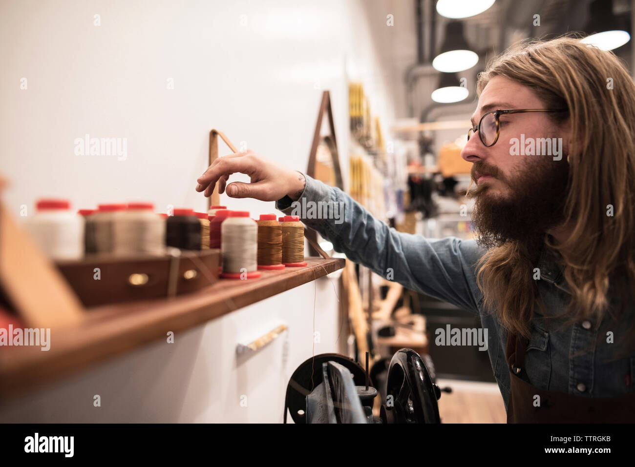 Shoemaker choosing spool on shelf at workshop Stock Photo