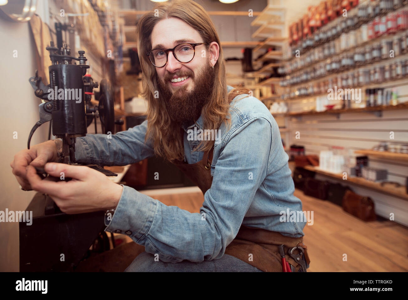 Portrait of smiling shoemaker working at sewing machine in workshop Stock Photo