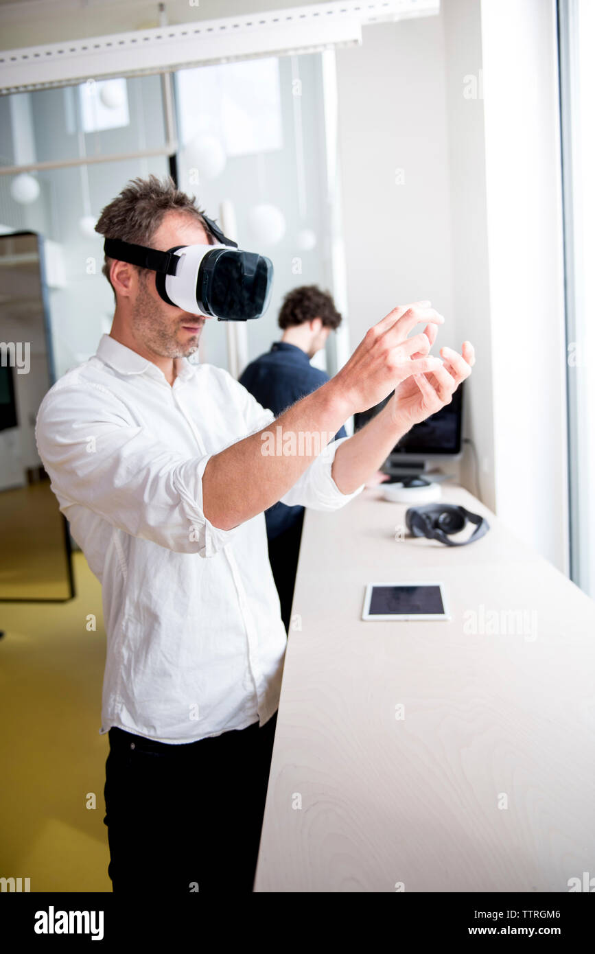 Engineer examining virtual reality simulator while coworker using computer at table Stock Photo