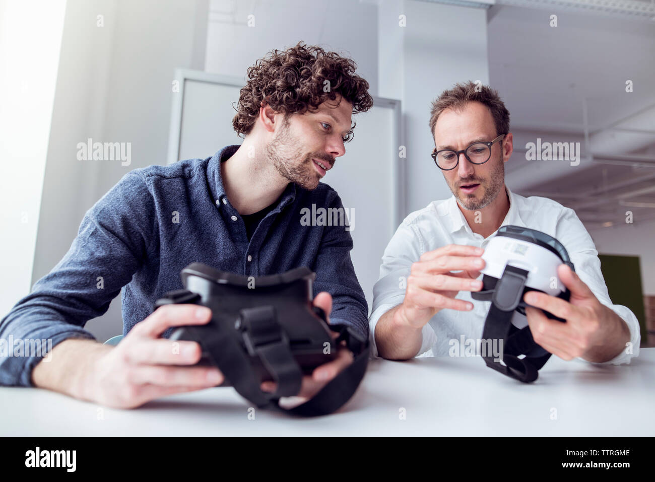 Technicians examining virtual reality simulators while sitting at table in office Stock Photo