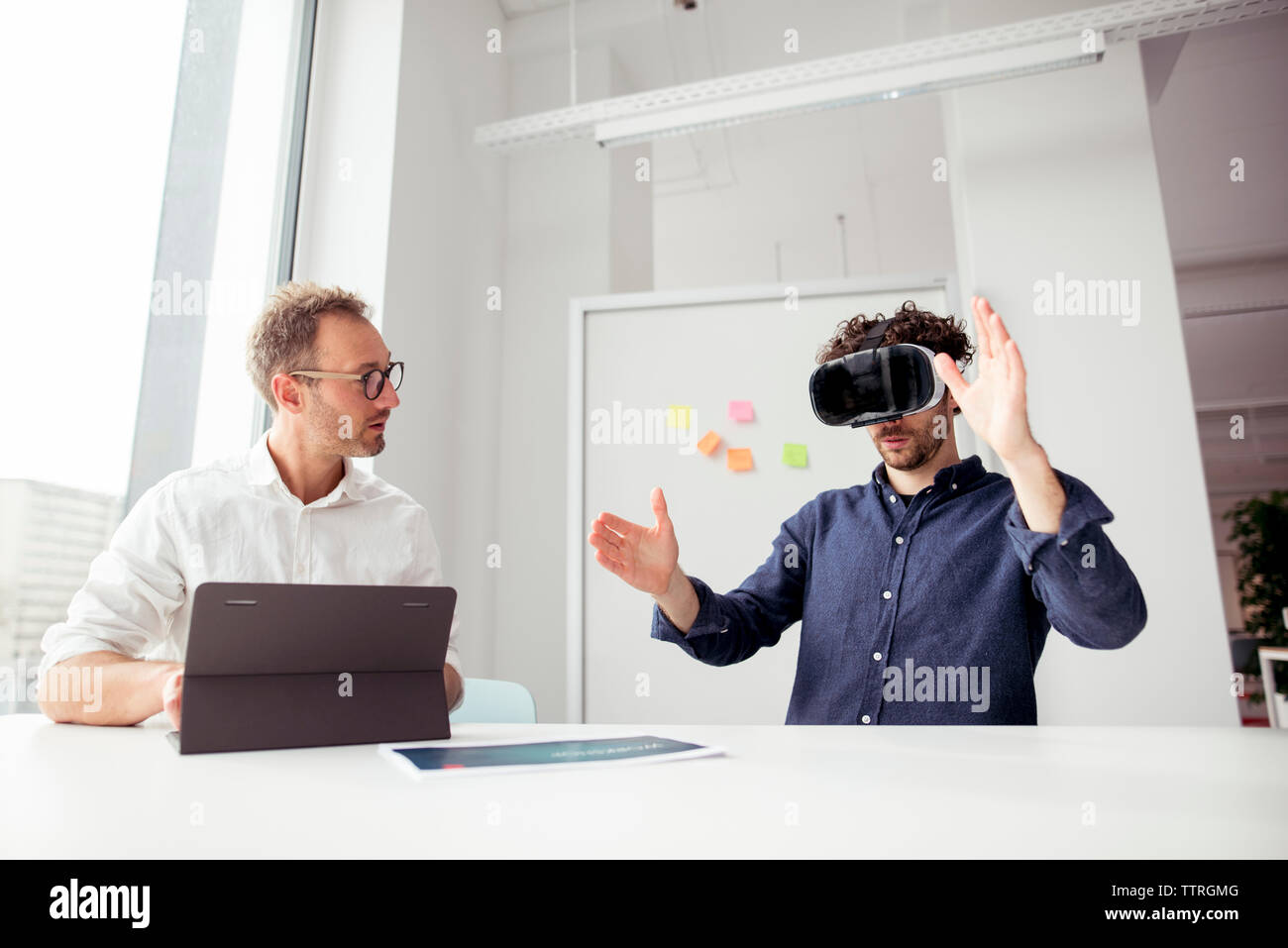 Engineer with tablet computer looking at coworker examining virtual reality simulator in office Stock Photo