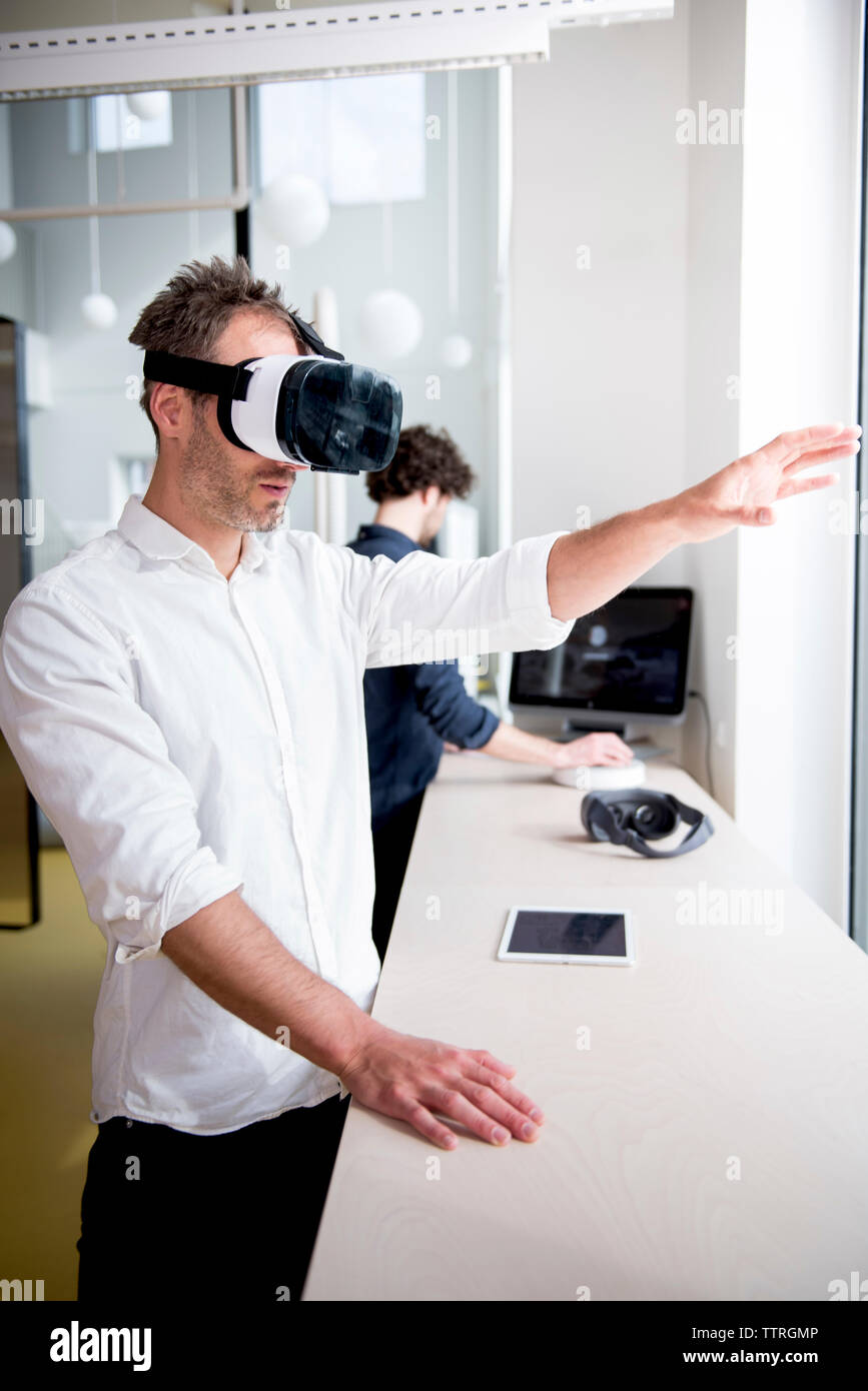 businessman examining virtual reality simulator while coworker using computer in office Stock Photo