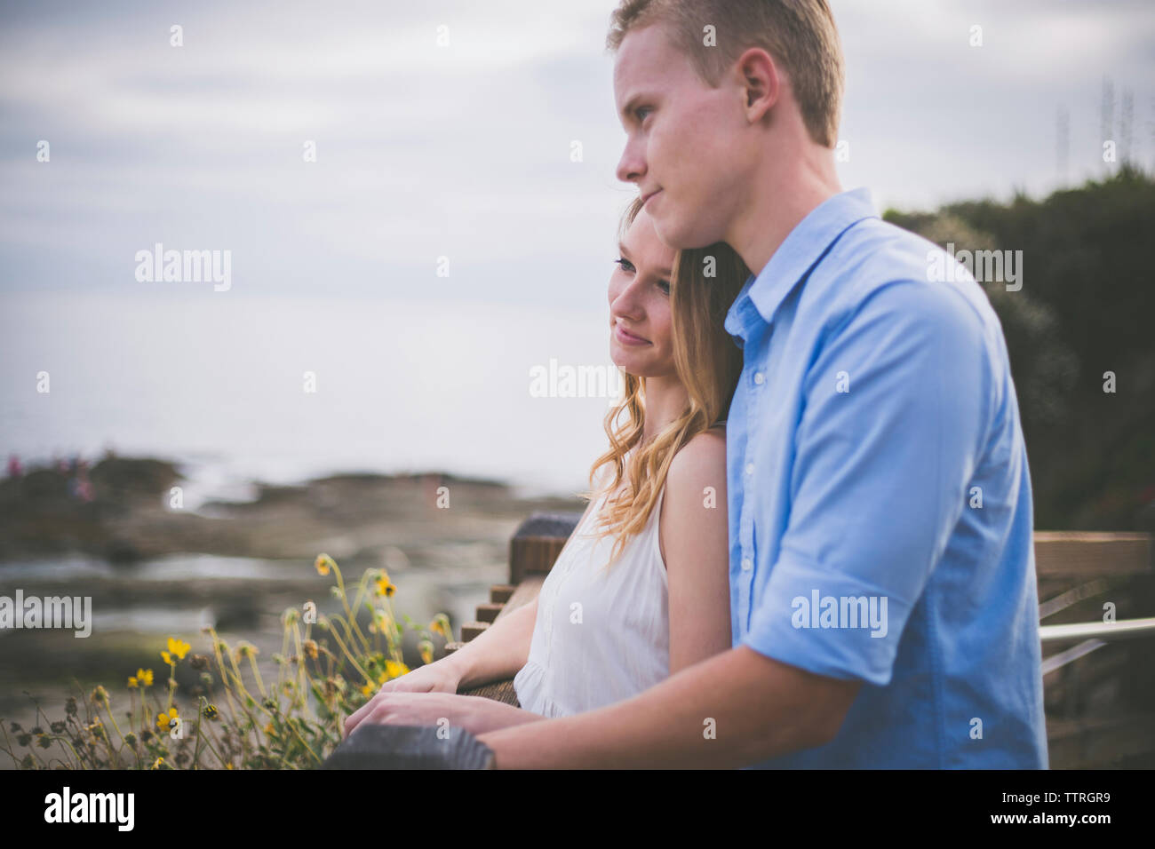 Smiling couple looking away while standing by railing against cloudy sky Stock Photo