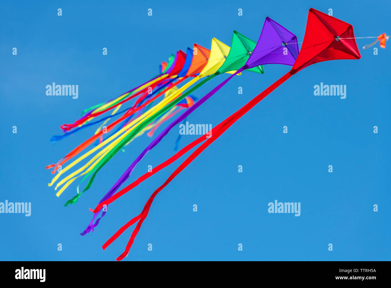 A row of colourful kites on a single line against a clear blue sky. Stock Photo