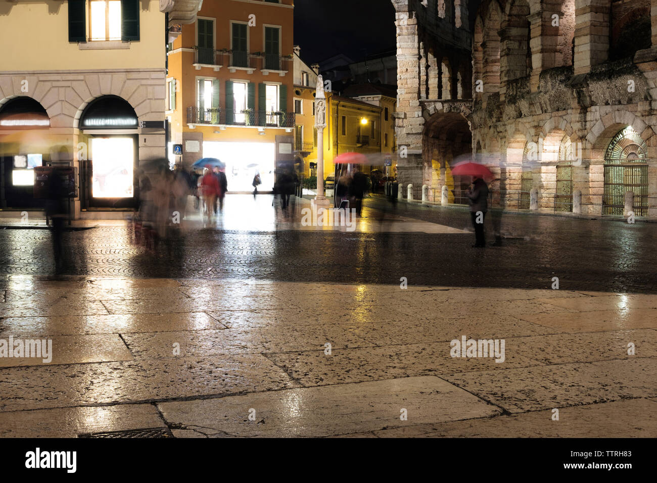 Blurred motion of people with umbrella in illuminated city during ...