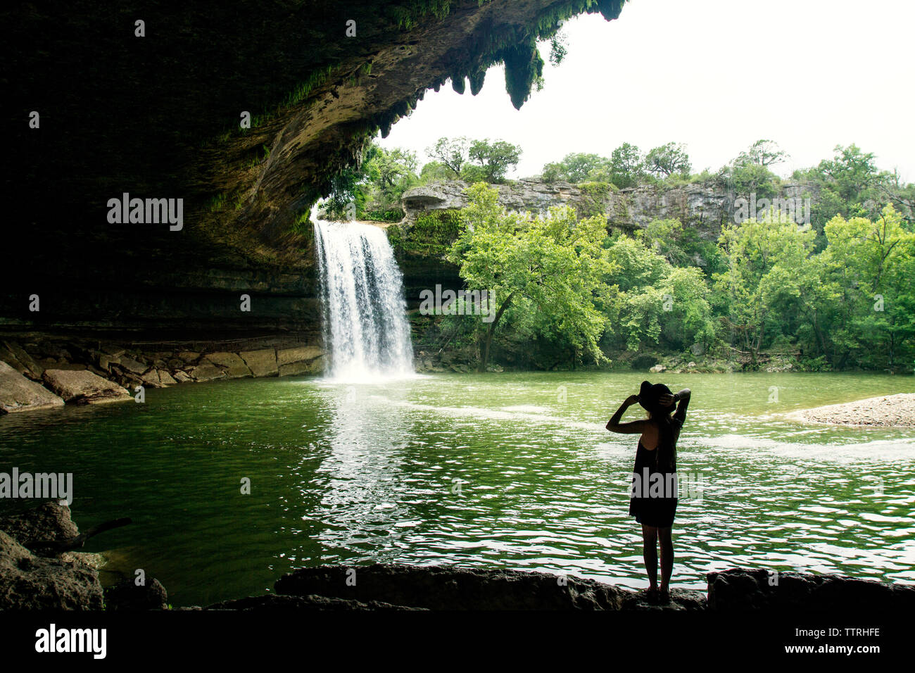 Woman looking at scenic waterfall in forest against clear sky Stock Photo